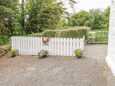 A white picket fence with a rooster decoration and flower pots on gravel at Cartron Cottage in Ballintubber County Mayo
