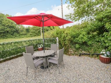 An outdoor seating area with a round table four chairs and a red umbrella on gravel at Cartron Cottage in Ballintubber County Mayo