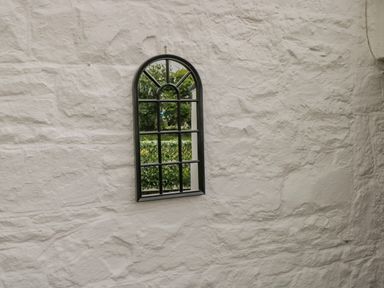 An arched mirror with a black frame hanging on a textured white stone wall at Cartron Cottage in Ballintubber County Mayo