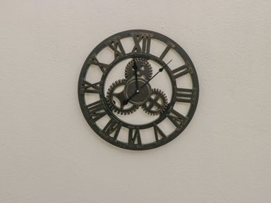 A round wall clock with Roman numerals and visible gears on a plain wall at Cartron Cottage in Ballintubber County Mayo