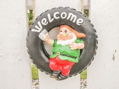 A garden gnome holding a book inside a black tire wreath with welcome text on a white wooden fence at Cartron Cottage in Ballintubber County Mayo