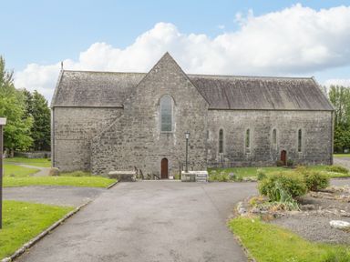 A stone building with arched windows and small doors surrounded by grass and pathways at Cartron Cottage in Ballintubber County Mayo