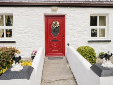 Front entrance with a red door flanked by white walls and eagle statues at Cartron Cottage Ballintubber County Mayo