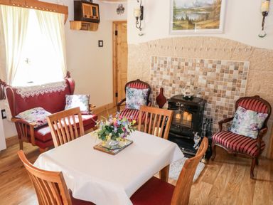 A dining area with wooden table and chairs a red loveseat two armchairs with striped upholstery a stove and tiled wall at Cartron Cottage Ballintubber County Mayo