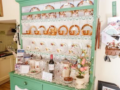 A green wooden cabinet with shelves holding decorative plates cups pitchers and a bottle of wine at Cartron Cottage Ballintubber County Mayo