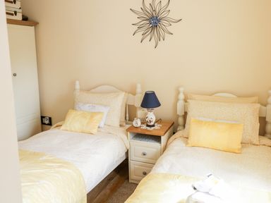 A bedroom with two single beds yellow bedding a nightstand with a lamp and clock and a flower wall decoration at Cartron Cottage in Ballintubber County Mayo