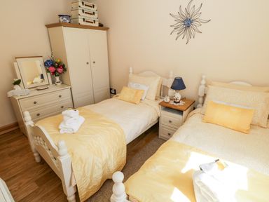 A bedroom with two single beds yellow bedding a nightstand with a lamp a wardrobe and a dresser with flowers at Cartron Cottage in Ballintubber County Mayo
