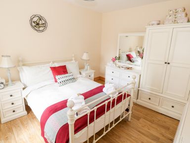 A bedroom with a bed with red and white bedding two bedside tables with lamps a dresser with a mirror and a wardrobe at Cartron Cottage in Ballintubber County Mayo