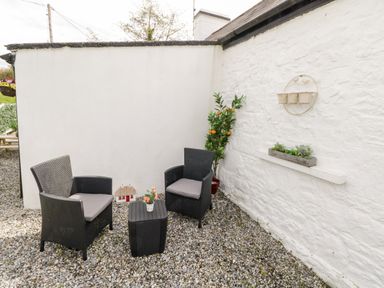 An outdoor seating area with two black chairs and a small table on gravel at Cartron Cottage in Ballintubber County Mayo