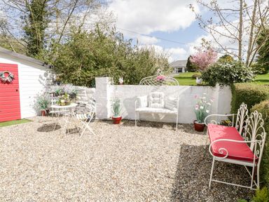 An outdoor patio with white metal chairs and benches with cushions and potted plants at Cartron Cottage in Ballintubber County Mayo