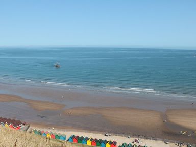 A beach with colorful beach huts on the shore and a boat on the water at Stoker's Rest in Whitby
