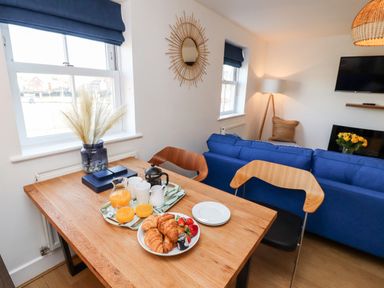 A dining table with croissants and juice in a living room with blue sofa and television at Stoker's Rest in Whitby