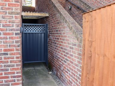 A narrow passageway between brick walls with a blue metal gate and a wooden fence at Stoker's Rest in Whitby