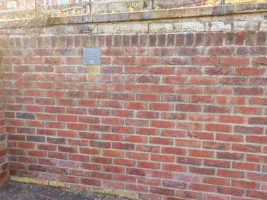 A red brick wall with a small sign on it and a paved ground at Stoker's Rest in Whitby