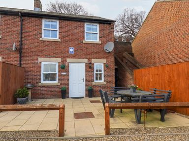 A brick house with white door and windows a patio with outdoor table and benches and wooden fences at Stoker's Rest in Whitby