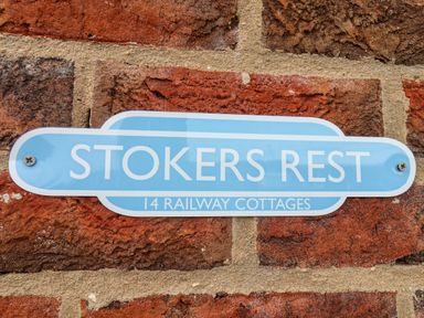 A blue sign with white text reading Stokers Rest 14 Railway Cottages on a brick wall at Stokers Rest in Whitby