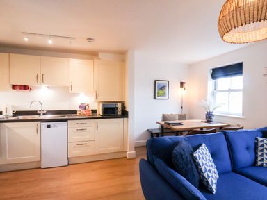 A kitchen area with white cabinets and black countertop next to a dining table and blue sofa at Stoker's Rest Whitby