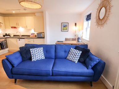 A blue sofa with patterned and plain cushions in a living area next to a kitchen and dining table at Stoker's Rest in Whitby
