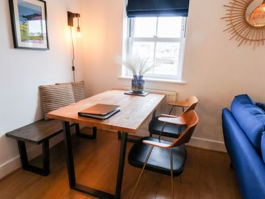 A dining area with a wooden table chairs a bench with cushions a window and a blue sofa at Stoker's Rest in Whitby