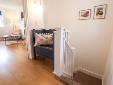 A hallway with stair railing a blue bench with a cushion and two framed pictures on the wall at Stoker's Rest in Whitby
