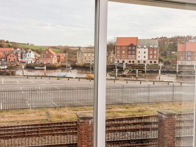 View through window with metal fence and railway tracks in foreground and houses near water in background at Stoker's Rest in Whitby