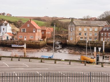 A harbor with boats docked near brick and stone buildings and a parking lot in the foreground at Stoker's Rest in Whitby