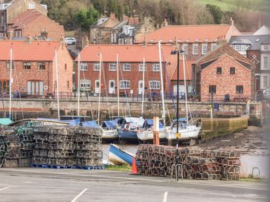 A harbor with fishing traps stacked on the ground boats moored along a waterfront and brick houses with tiled roofs in the background at Stoker's Rest in Whitby