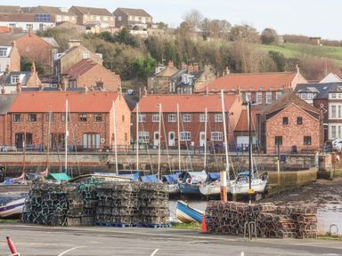 A harbor with stacks of lobster pots and boats moored by brick buildings at Stoker's Rest in Whitby