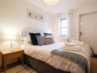 A bedroom with a double bed with pillows and folded towels a side table with a lamp a window with curtains and a door at Stoker's Rest in Whitby