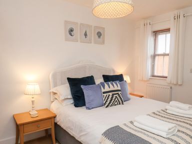 A bedroom with a double bed two bedside tables with lamps a window with curtains and framed pictures on the wall at Stoker's Rest in Whitby