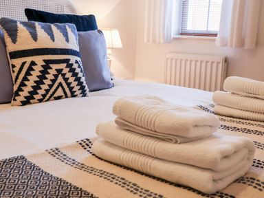 A bed with folded white towels and patterned cushions near a window at Stokers Rest in Whitby