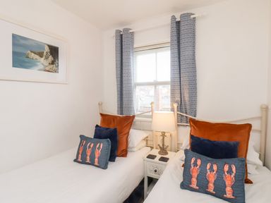A bedroom with two single beds a nightstand with a lamp and window with patterned curtains at Stoker's Rest in Whitby