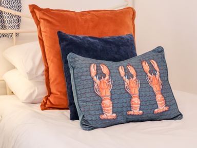 Three decorative pillows on a white bed including one with lobster designs at Stoker's Rest in Whitby