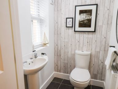 A bathroom with a toilet sink and window with blinds and framed pictures on a wooden paneled wall at Stoker's Rest in Whitby