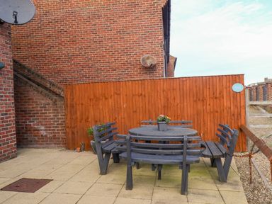 An outdoor patio with a round wooden table and matching benches against a wooden fence at Stoker's Rest in Whitby