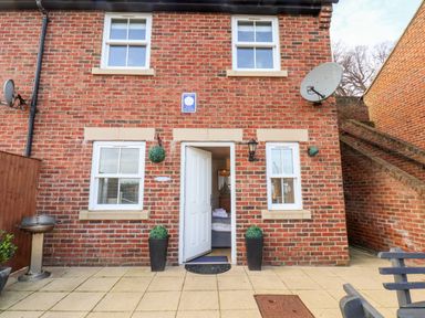 A brick house with four white framed windows and an open white door with two tall plant pots outside at Stoker's Rest in Whitby