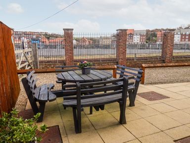 A patio with a round wooden table and four matching benches with a flower pot on the table at Stoker's Rest in Whitby