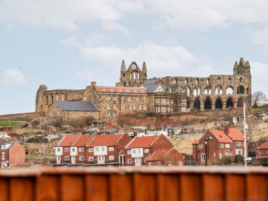 A historic stone abbey on a hill above houses with red roofs in Whitby