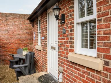 An outdoor area with a white door, two windows, black wall lamp, wooden table and chairs with a plant on the table at Stoker's Rest in Whitby