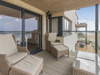 A balcony with cushioned wicker chairs and a glass table overlooking the beach at Apartment 18 Burgh Island Causeway Bigbury-On-Sea
