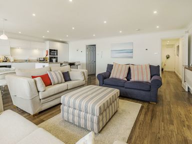A living room with sofas and a striped ottoman next to a kitchen area at Apartment 18 Burgh Island Causeway in Bigbury-On-Sea