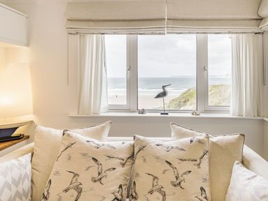 A sofa with bird patterned cushions facing a window with a view of the beach and sea at Apartment 18 Burgh Island Causeway in Bigbury-On-Sea
