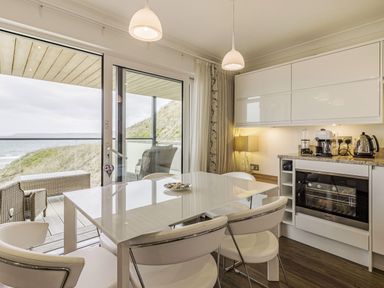A kitchen dining area with white furniture and appliances overlooking a balcony with wicker chairs and a sea view at Apartment 18 Burgh Island Causeway