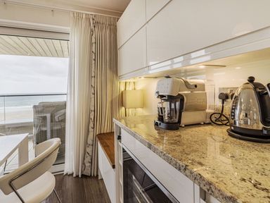 A kitchen countertop with a coffee machine and kettle near a window showing a balcony and beach at Apartment 18 Burgh Island Causeway Bigbury-On-Sea