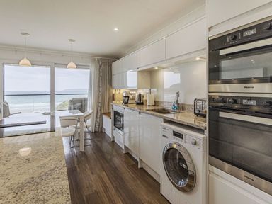A kitchen with white cabinets washing machine oven and dining table with chairs near windows showing sea view at Apartment 18 Burgh Island Causeway in Bigbury-On-Sea