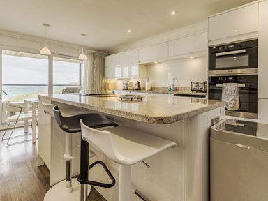 A kitchen with a large island, bar stools, ovens, and large windows showing an outdoor view at Apartment 18 Burgh Island Causeway in Bigbury-On-Sea