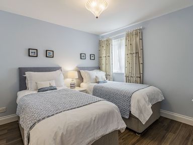 A bedroom with two single beds a lamp between the beds and a window with curtains at Apartment 18 Burgh Island Causeway in Bigbury-On-Sea