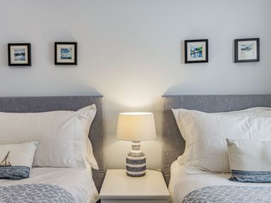 Two beds with grey headboards white bedding and a lamp on a nightstand between them at Apartment 18 Burgh Island Causeway in Bigbury-On-Sea