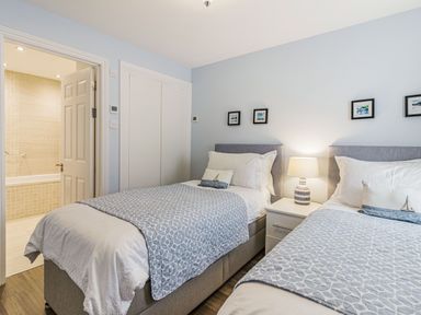 A bedroom with two single beds a bedside table with a lamp and a bathroom visible through an open door at Apartment 18 Burgh Island Causeway in Bigbury-On-Sea