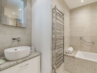 A bathroom with a sink on a marble countertop a mirror a towel rack and a bathtub with a rolled towel at Apartment 18 Burgh Island Causeway Bigbury-On-Sea